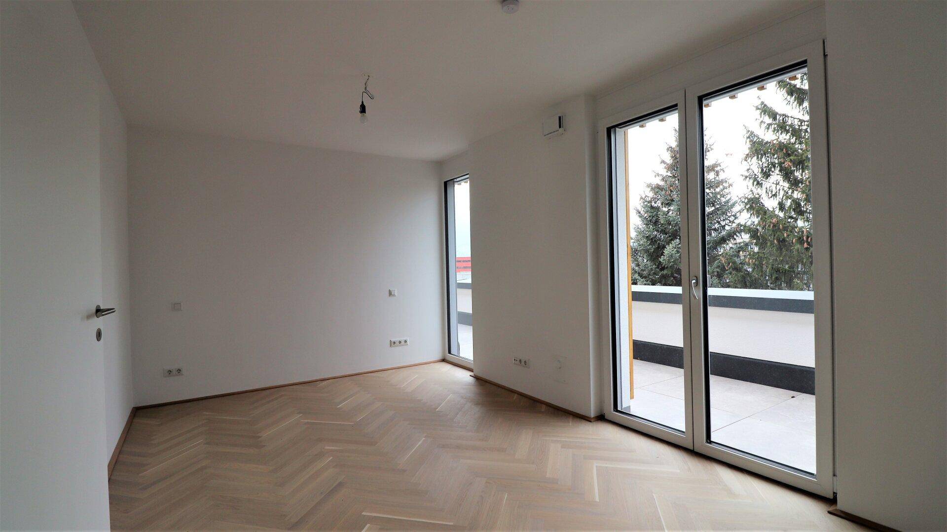 Helles Zimmer mit Fischgrätparkett und Zugang zu einer großen Terrasse.