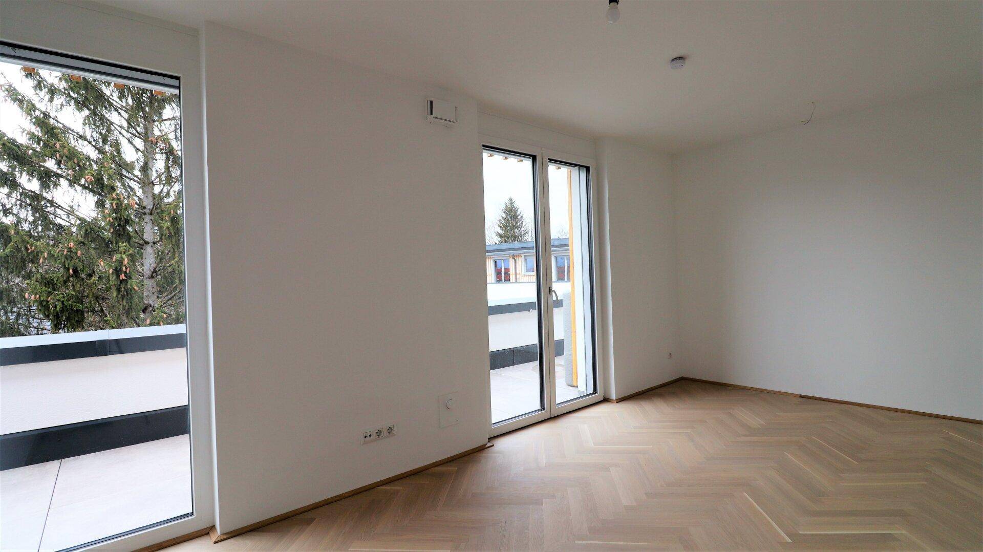 Lichtdurchflutetes Zimmer mit großen Fenstern und Zugang zur Außenterrasse.