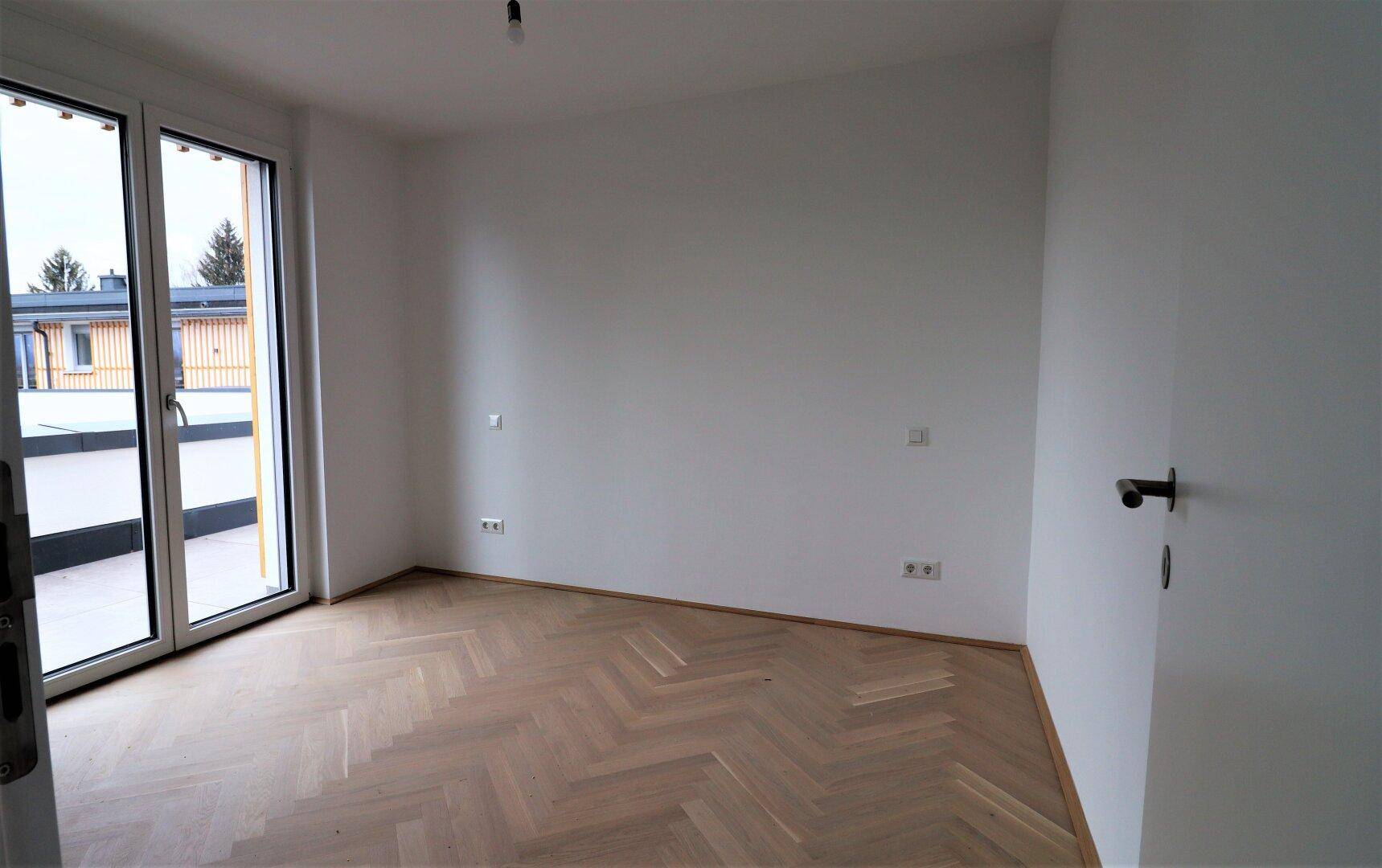 Geräumiges Zimmer mit hellem Fischgrätparkett und Zugang zur Terrasse.