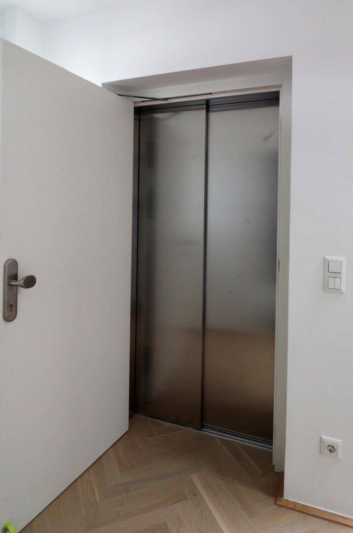 Heller Flur mit Parkettboden und Zugang zu einem modernen Aufzug.