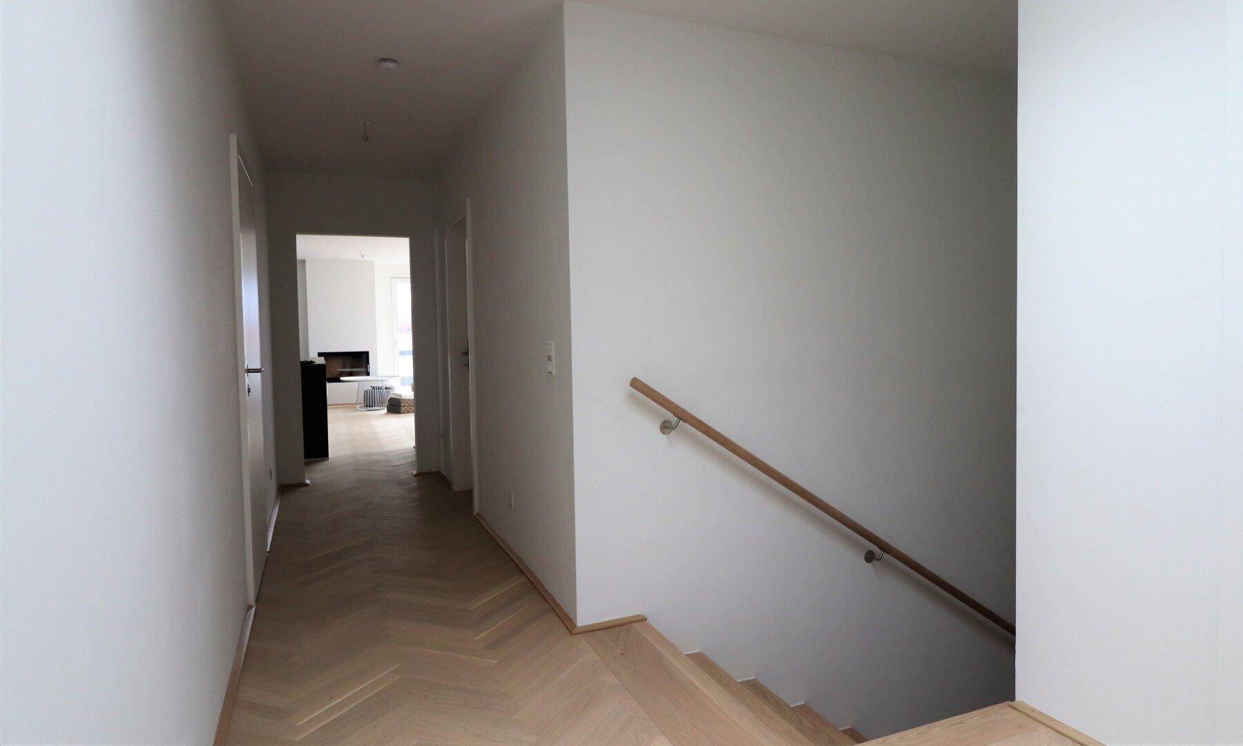 Langer Flur mit Fischgrätparkett und Treppenaufgang zu den Wohnbereichen.
