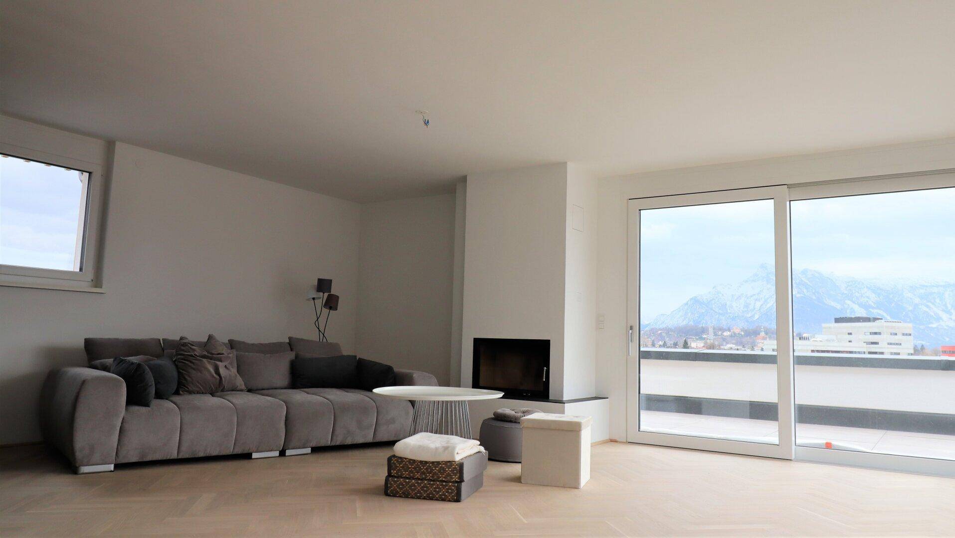 Helles Wohnzimmer mit Sofa, Kamin und großen Schiebetüren zur Terrasse mit Bergblick.