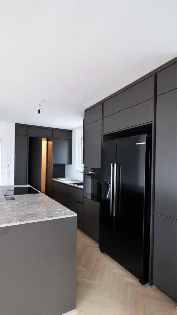 Moderne schwarze Einbauküche mit integrierten Geräten und großem Kühlschrank.