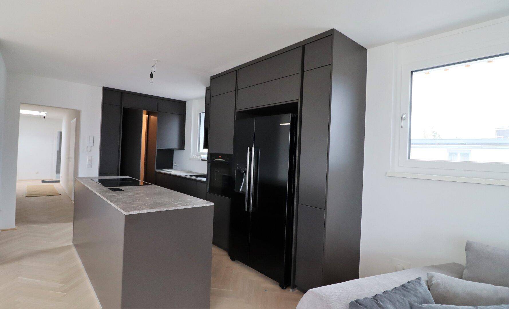 Offene Küche mit schwarzer Einbauküche, Kücheninsel und Blick in den Wohnbereich.