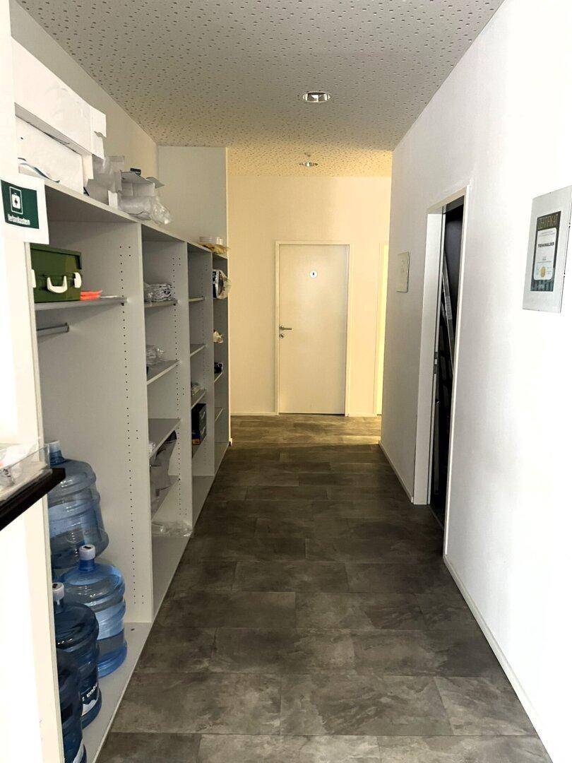 Langer, heller Flur mit Regalen für Lagerung und einer Tür am Ende, sauber und funktional.