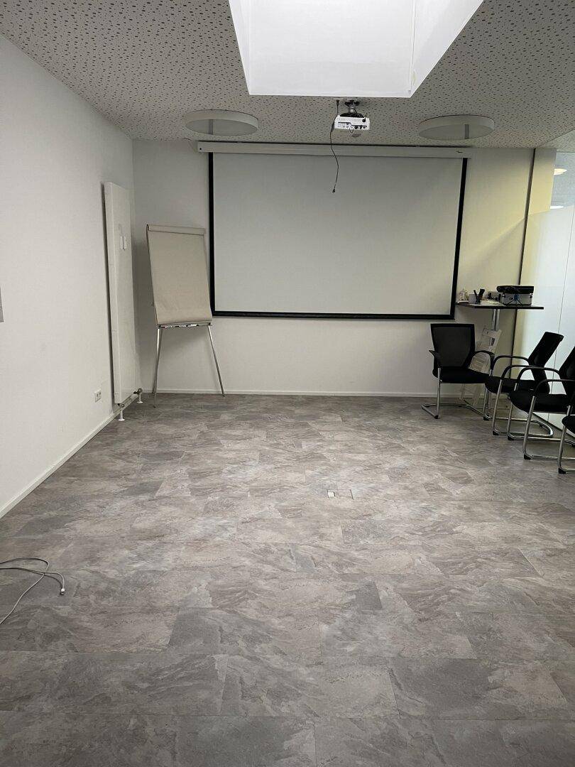 Geräumiger Konferenzraum mit Projektionsleinwand und Flipchart, bereit für Besprechungen und Schulungen.