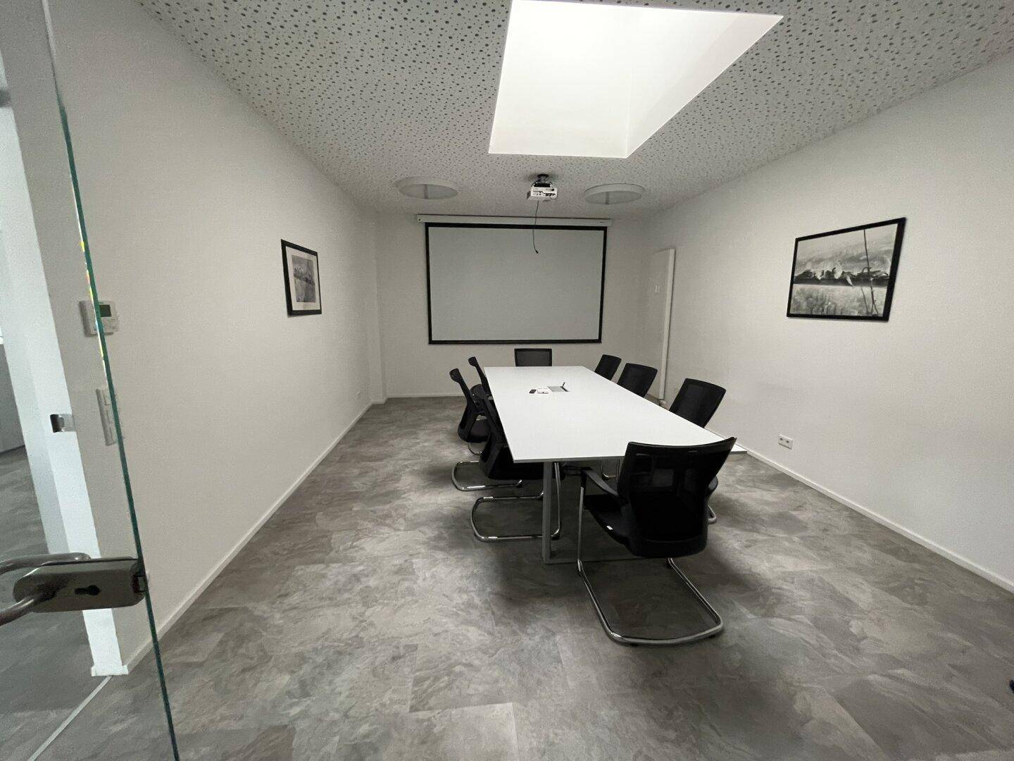 Konferenzraum mit großem Tisch, Projektor und Leinwand, ideal für Präsentationen und Besprechungen.