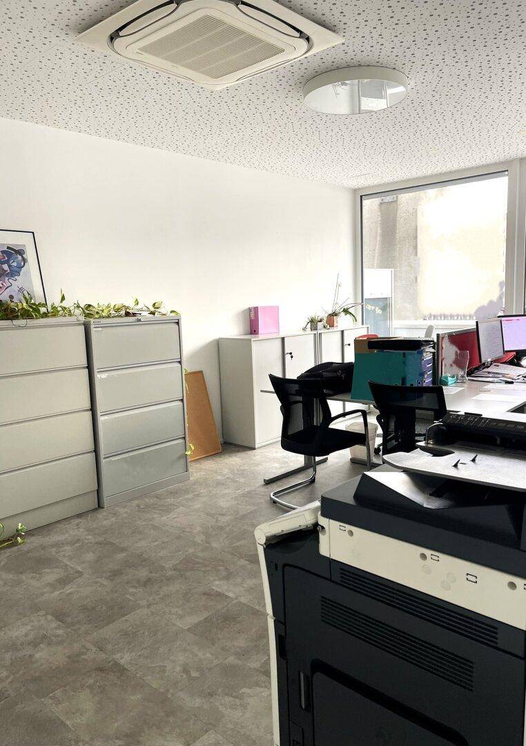 Detailansicht eines Bürobereichs mit Schränken, Arbeitsplatz und Klimaanlage, hell und funktional.