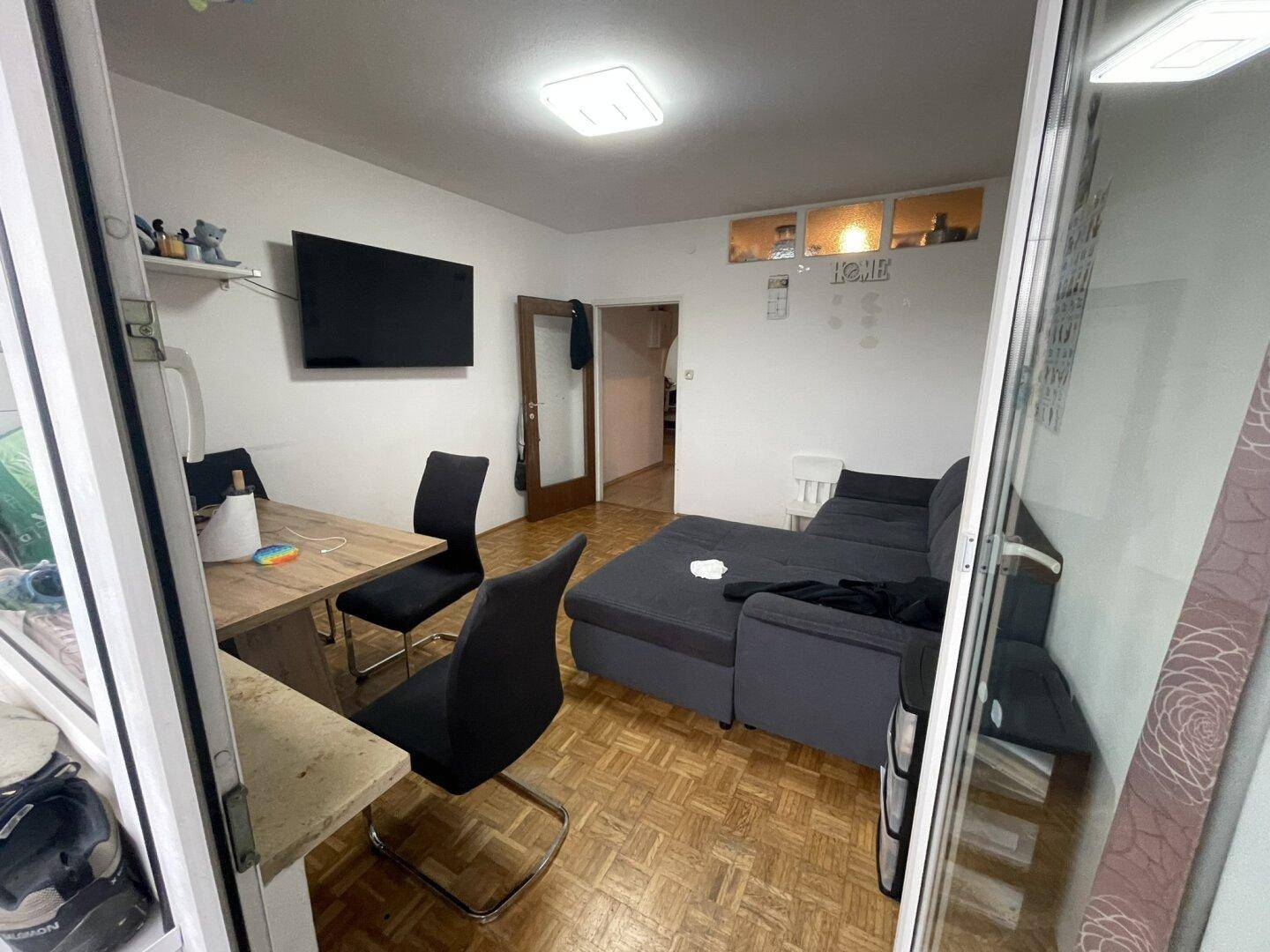 Gemütliches Wohnzimmer mit Sofa, Esstisch und Zugang zu einem Balkon oder Wintergarten.