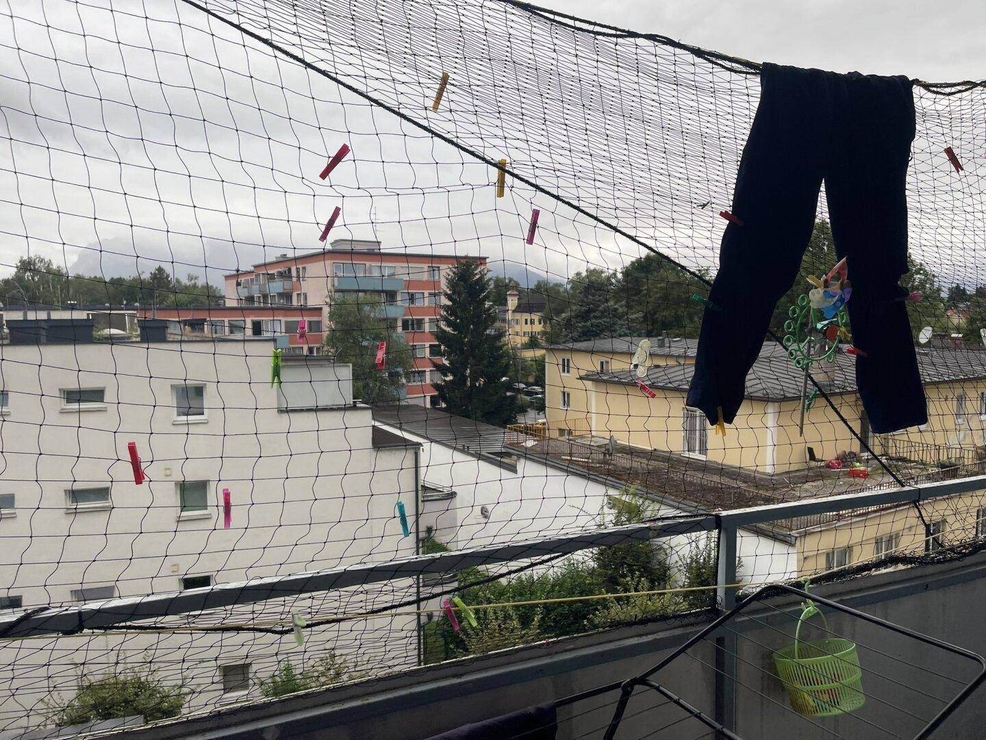 Balkon mit Wäscheleine und Blick auf die umliegenden Wohngebäude und Berge im Hintergrund.