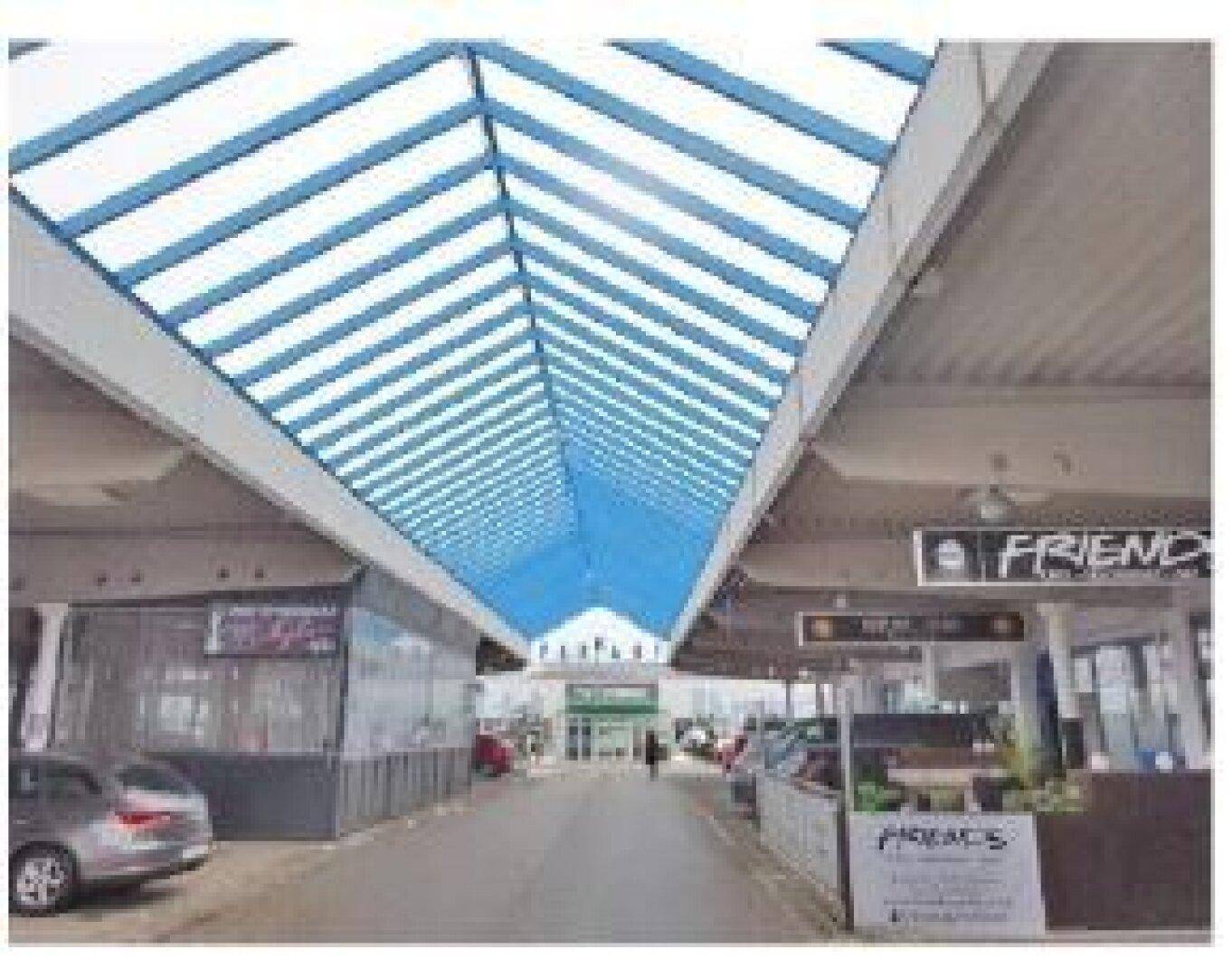 Überdachte Ladenpassage mit markantem blau-weiß gestreiftem Dach und verschiedenen Geschäften.