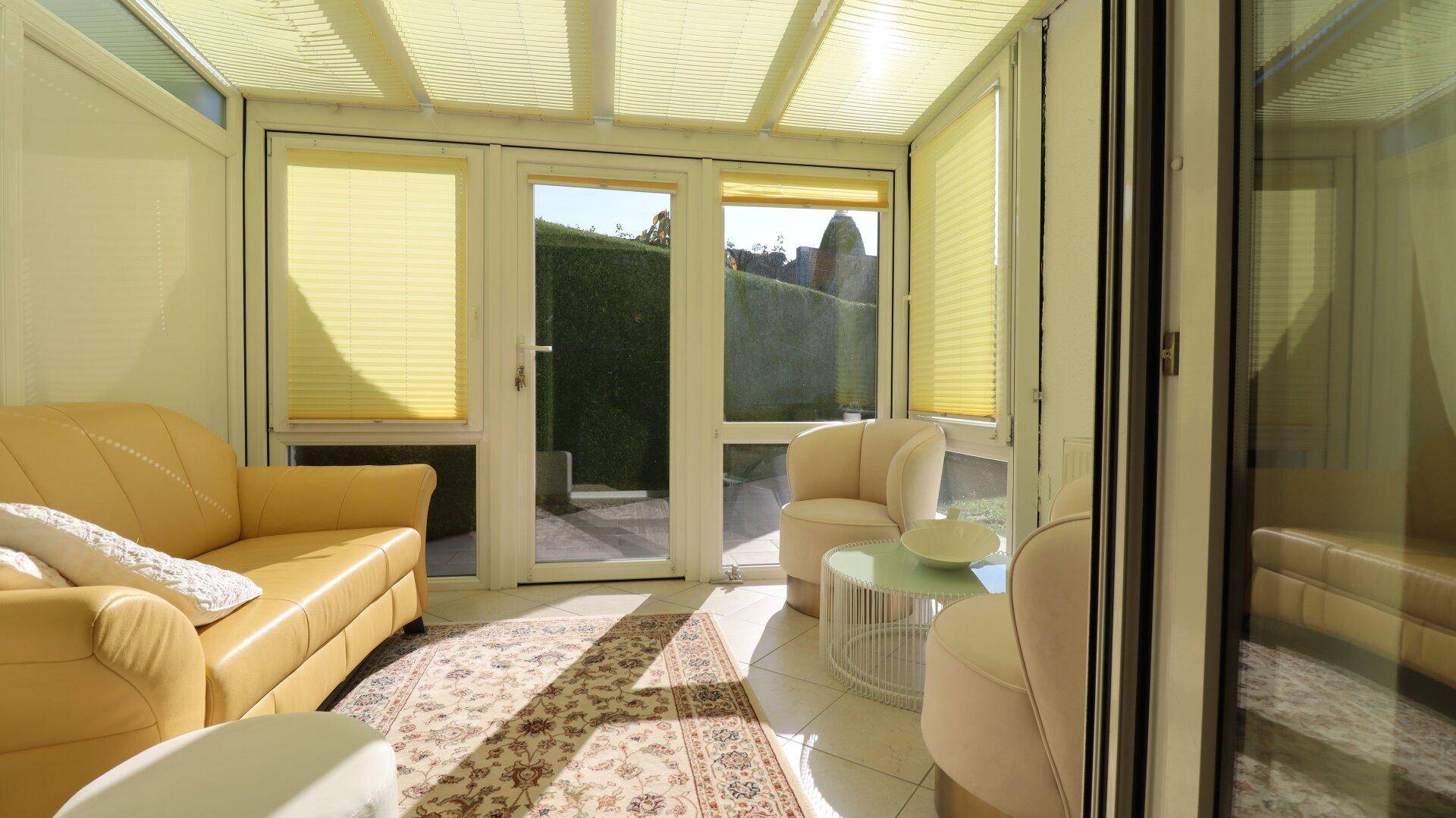 Gemütlicher Wintergarten mit bequemen Möbeln, Teppich und Blick ins Grüne.