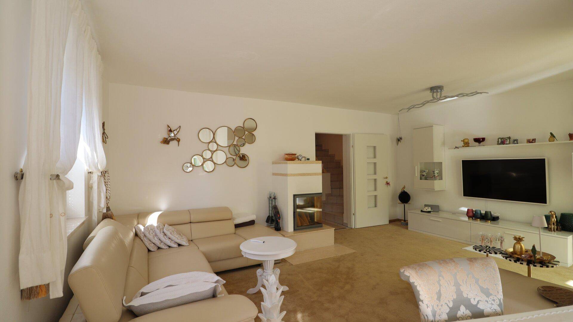 Geräumiger Wohnbereich mit beigem Sofa, Kamin und Zugang zur Treppe.