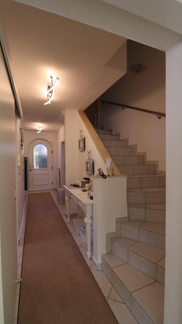 Heller Flur mit Treppenaufgang, Teppichläufer und Eingangstür im Hintergrund.