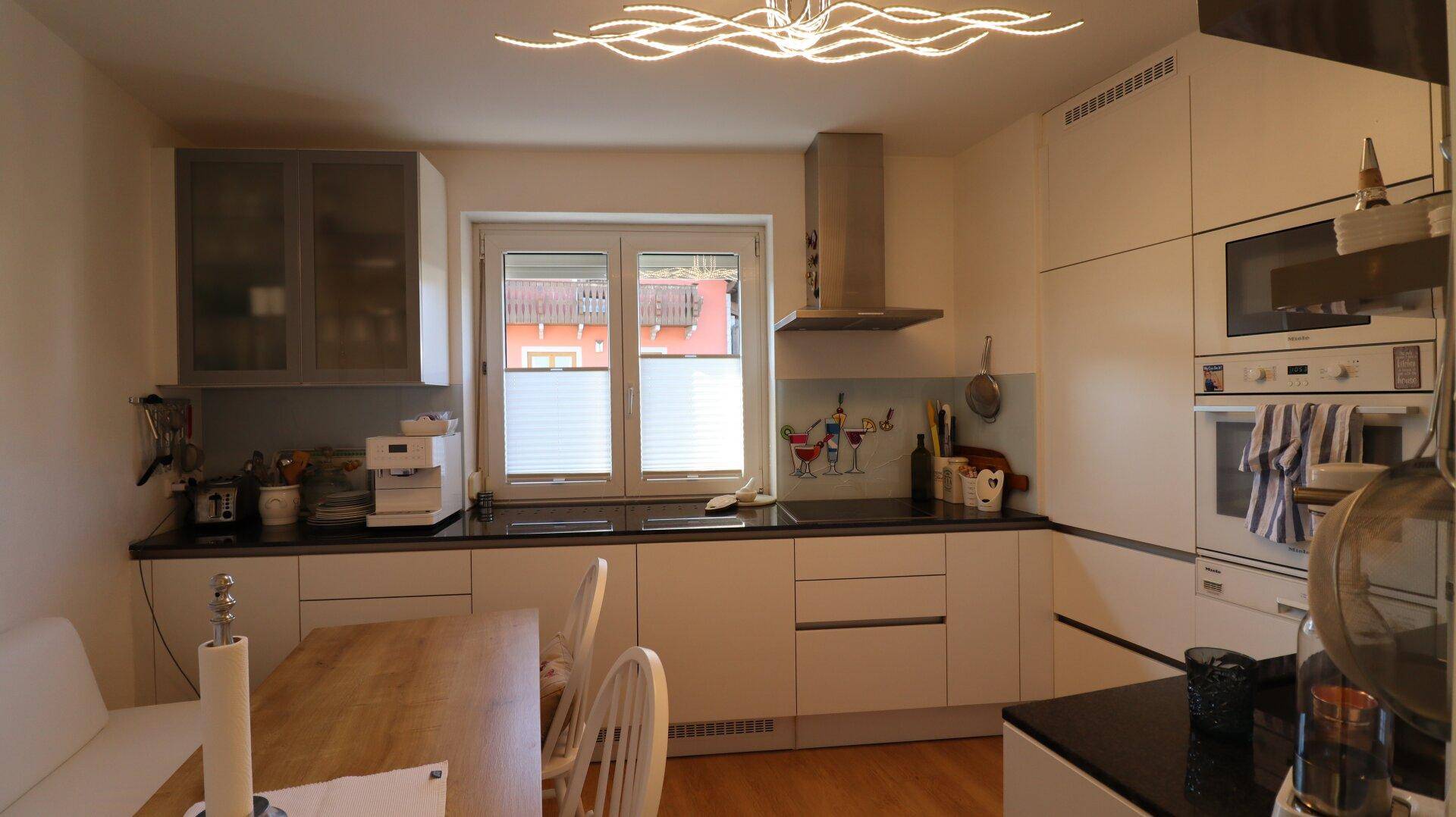 Moderne Einbauküche mit weißen Schränken, dunkler Arbeitsplatte und Fenster.