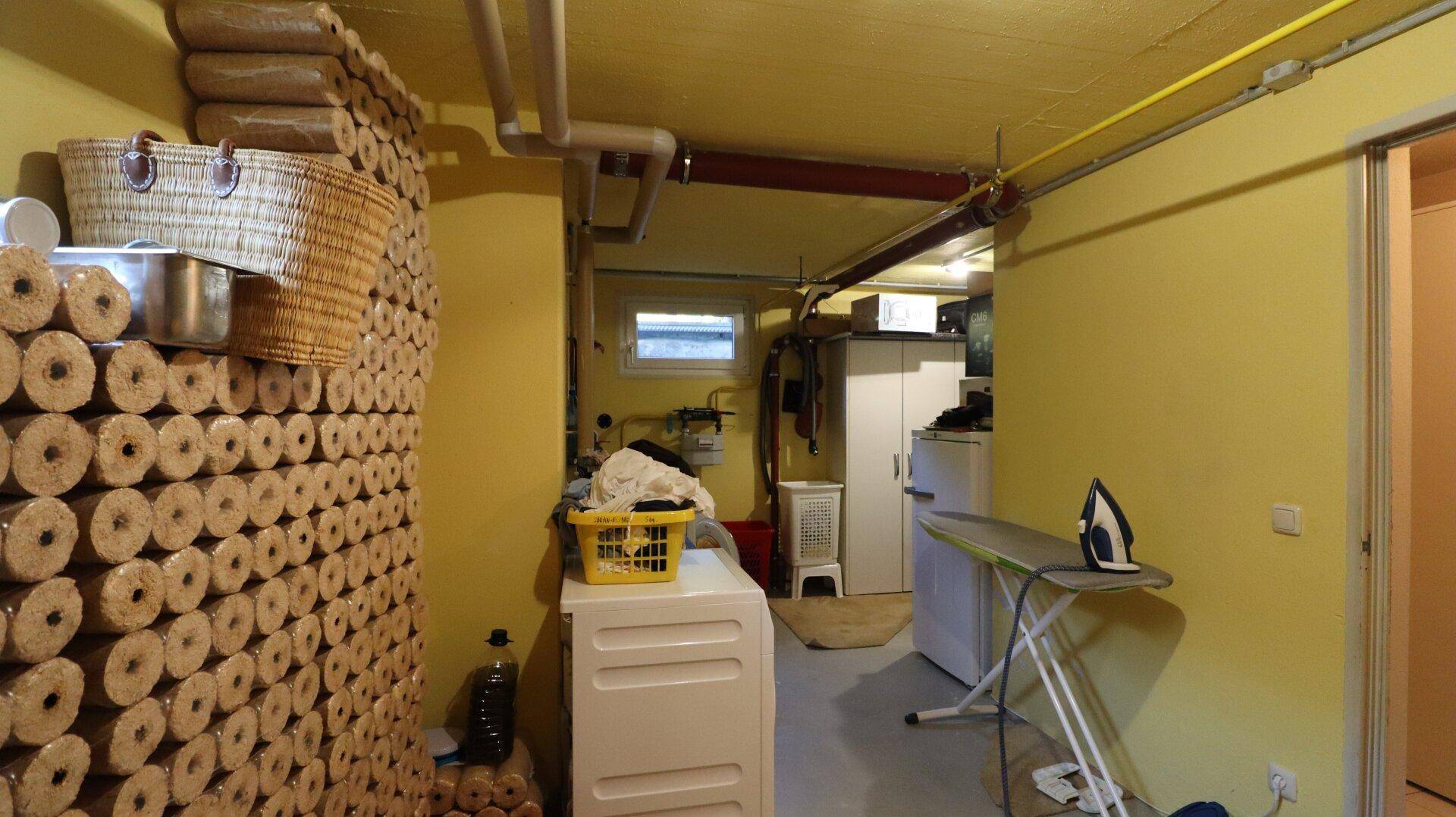 Waschküche im Keller mit Waschmaschine, Bügelbrett und Lagerfläche.