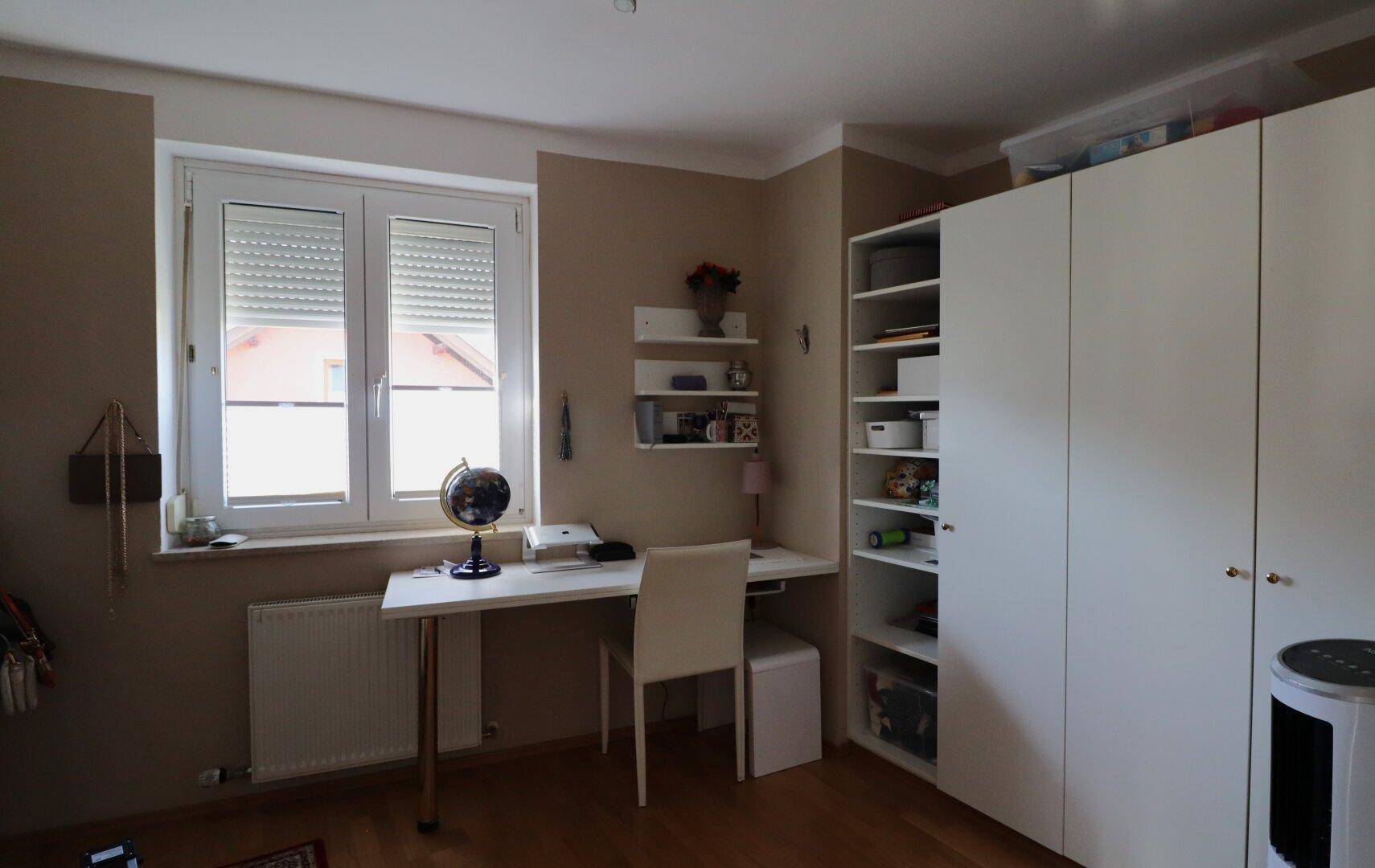 Arbeitszimmer mit Schreibtisch, Regal und Fenster für natürliches Licht.