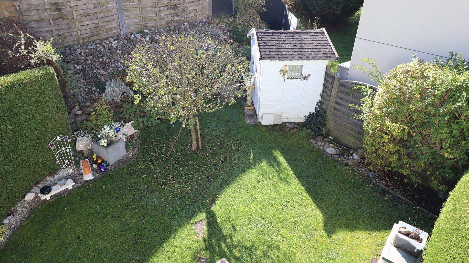 Gepflegter Garten mit Rasenfläche, Bäumen und einem kleinen Gartenhaus.