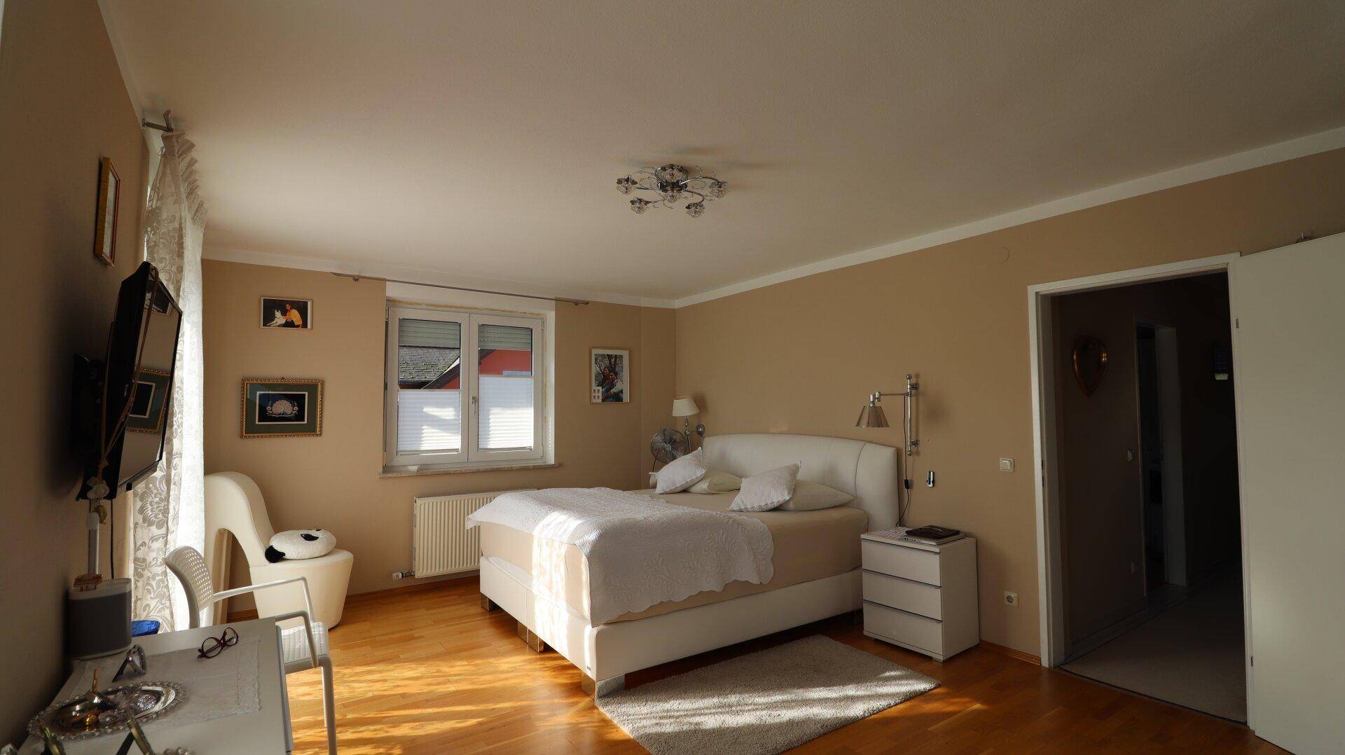 Helles Schlafzimmer mit Doppelbett, Holzfußboden und Fenster mit Blick ins Grüne.