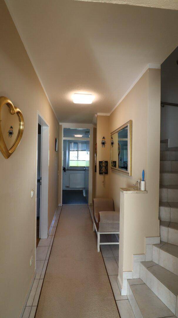 Heller Flur mit Teppichläufer, Spiegel und Zugang zu weiteren Räumen.