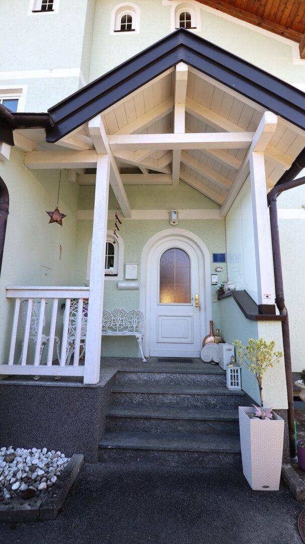 Eingangsbereich des Hauses mit überdachtem Vordach, Treppe und Bogenfenstern.