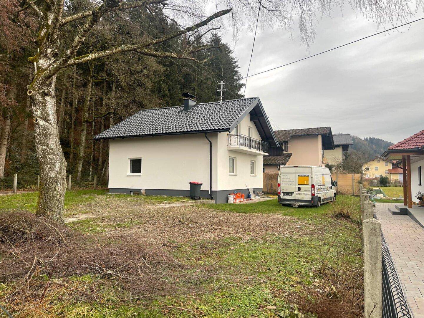 Rückansicht des Hauses mit Gartenbereich und angrenzendem Wald, unter bewölktem Himmel und mit Baumbestand.