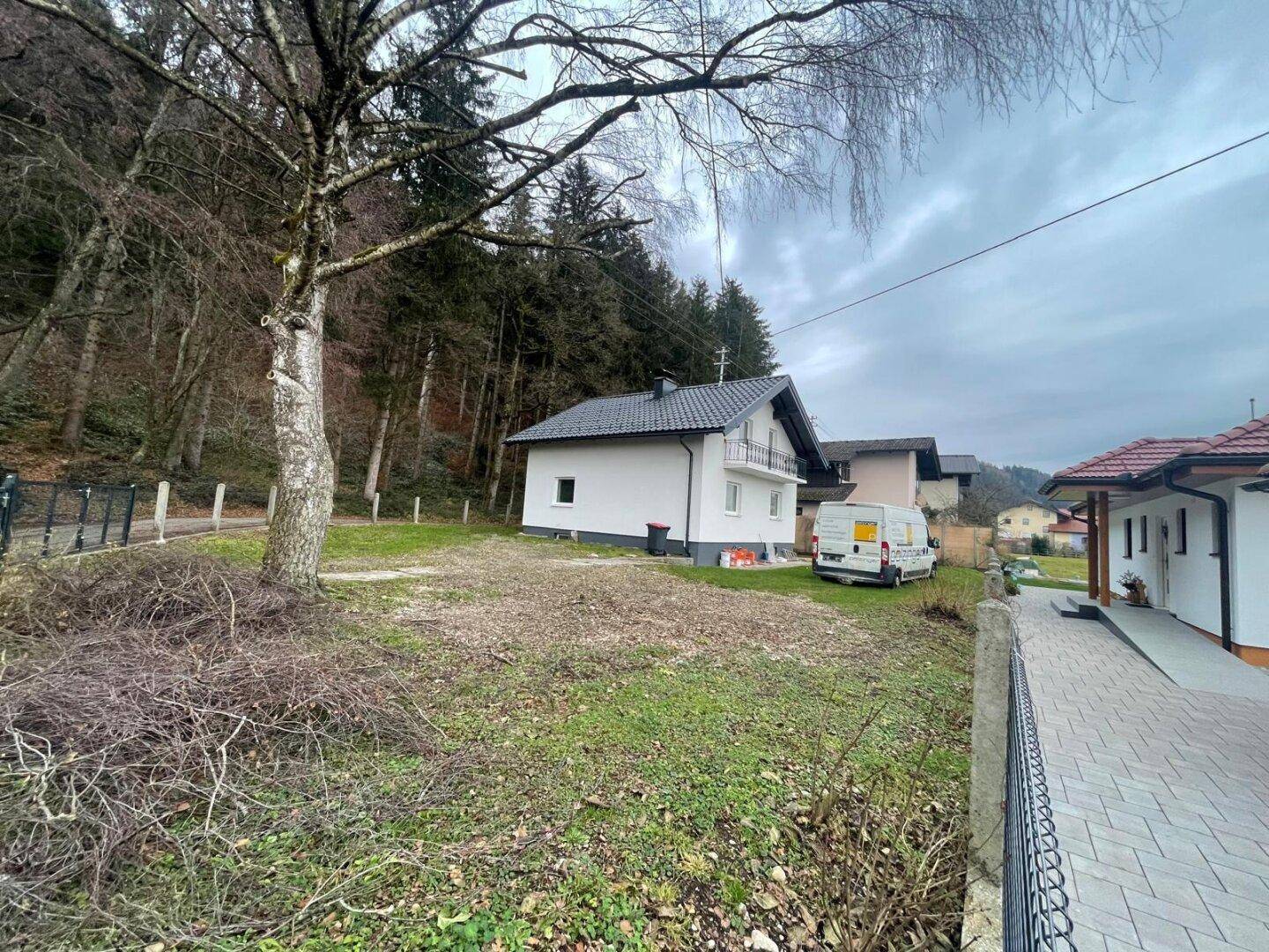 Haus in ländlicher Umgebung mit Wald im Hintergrund und einem großen, noch ungestalteten Gartenbereich.