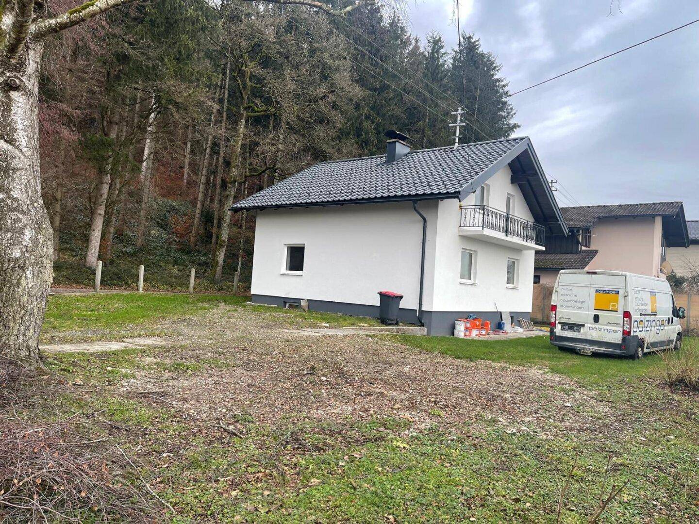 Haus in ländlicher Umgebung mit Wald im Hintergrund und einem großen, noch ungestalteten Gartenbereich.