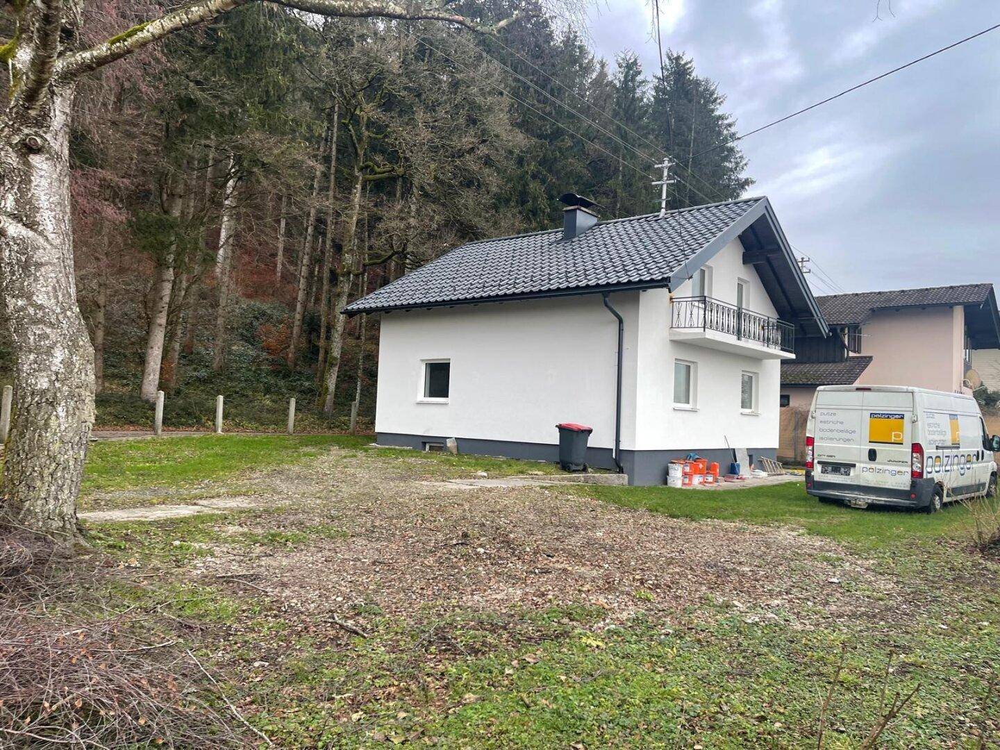Haus in ländlicher Umgebung mit Wald im Hintergrund und einem großen, noch ungestalteten Gartenbereich.