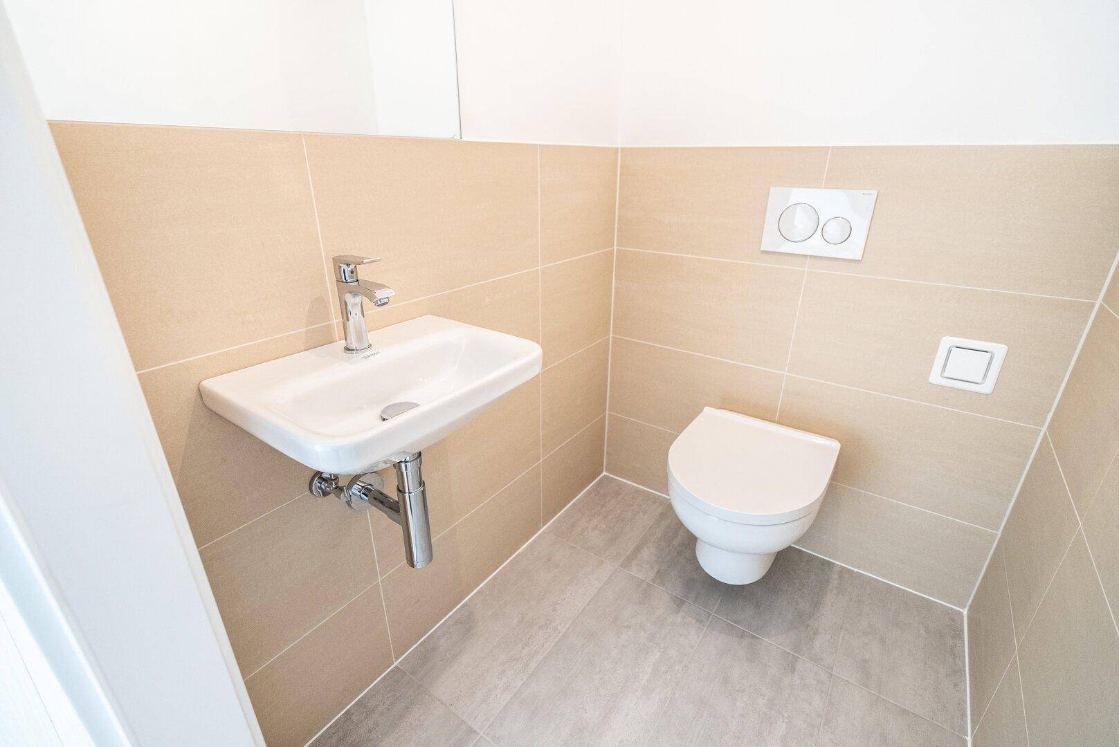 Kleines Gäste-WC mit Wand-WC und Waschbecken, hell gefliest und funktional.