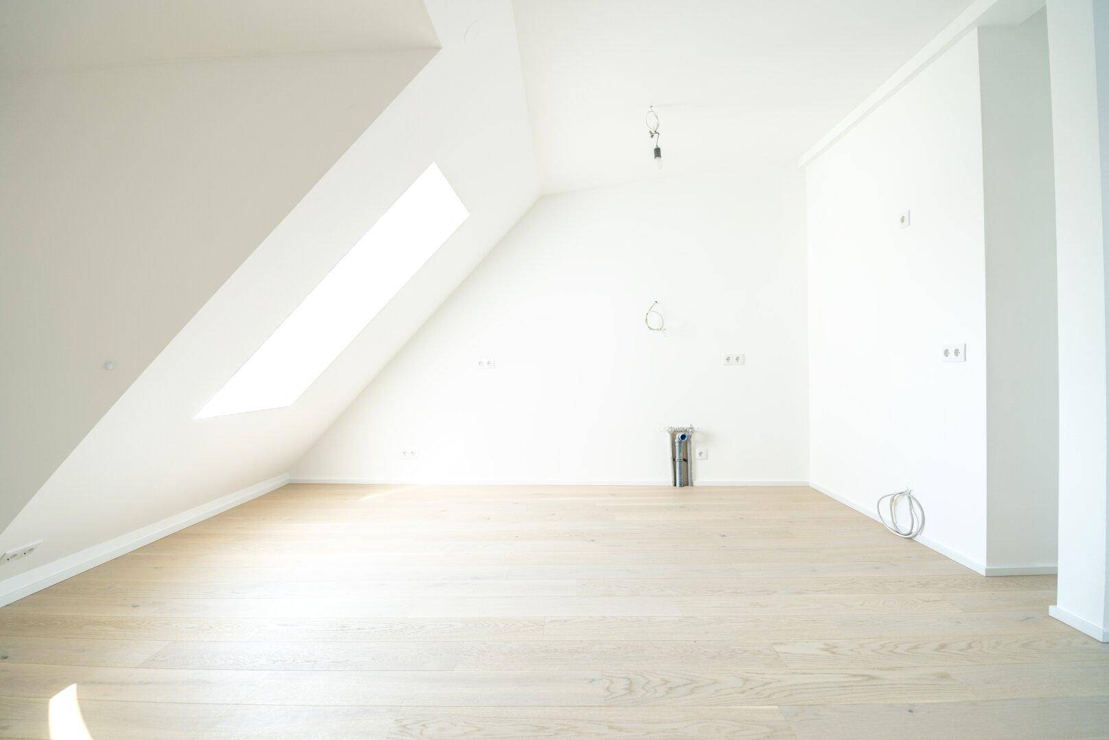 Heller Raum im Dachgeschoss mit Holzboden, schräger Wand und einem Dachfenster.