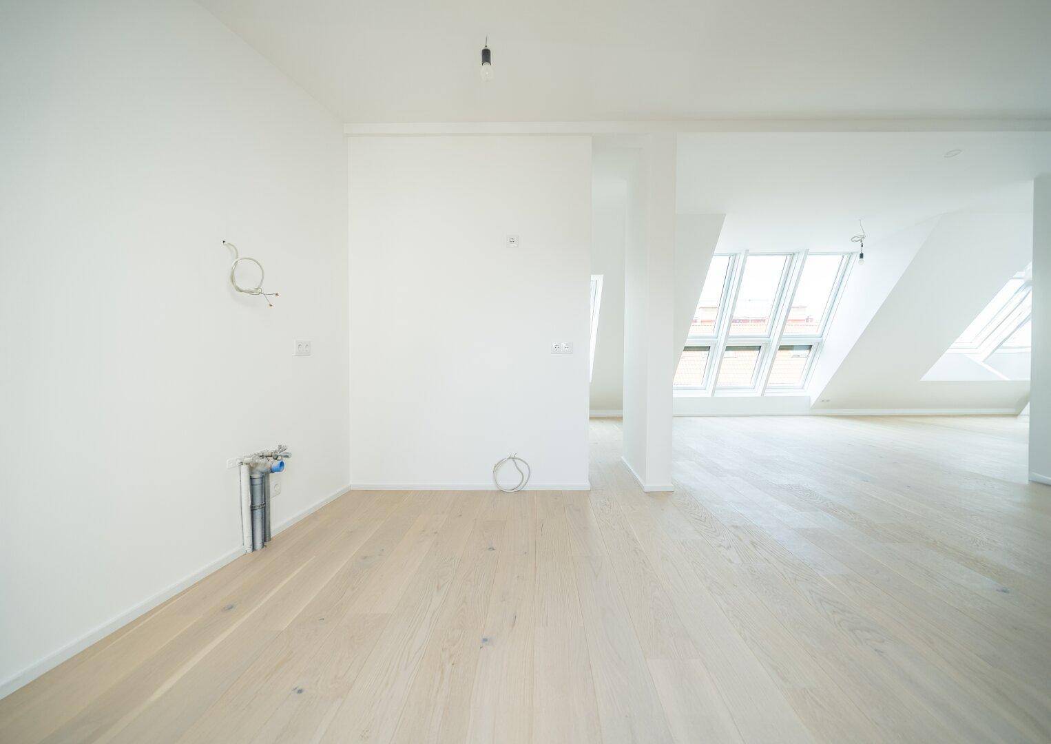 Offener, heller Raum im Dachgeschoss mit Holzboden und Vorinstallationen für eine Küche oder Bad.