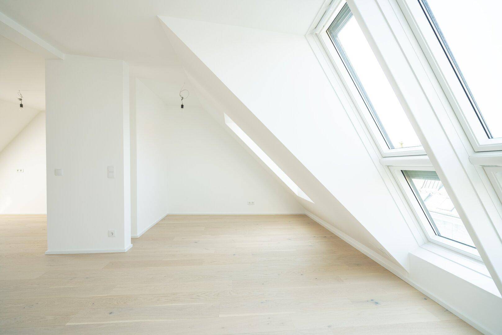 Geräumiger Wohnbereich im Dachgeschoss mit viel Tageslicht durch große, schräge Fenster.