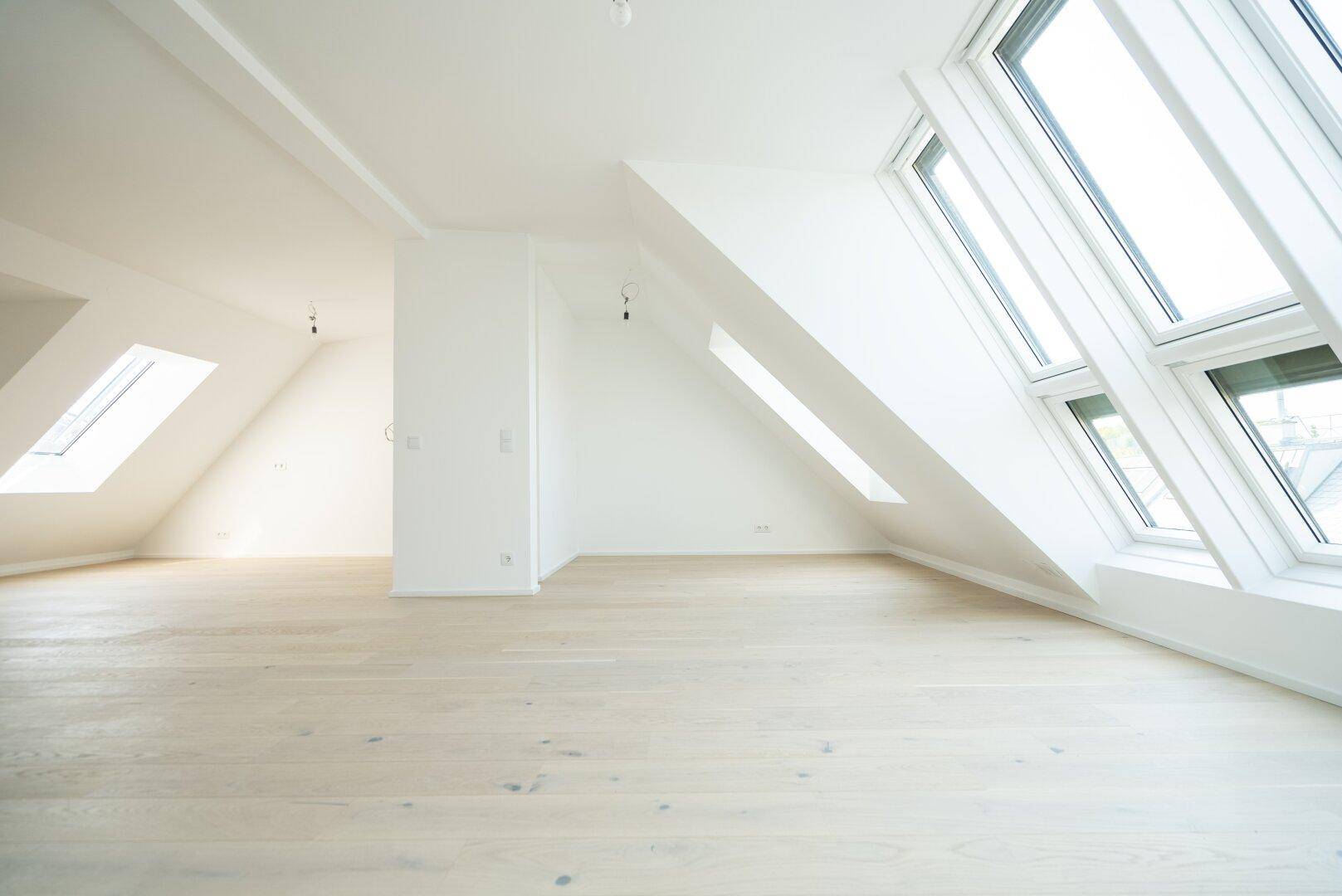 Lichtdurchfluteter Wohnbereich im Dachgeschoss mit schrägen Wänden und großen, modernen Dachfenstern.