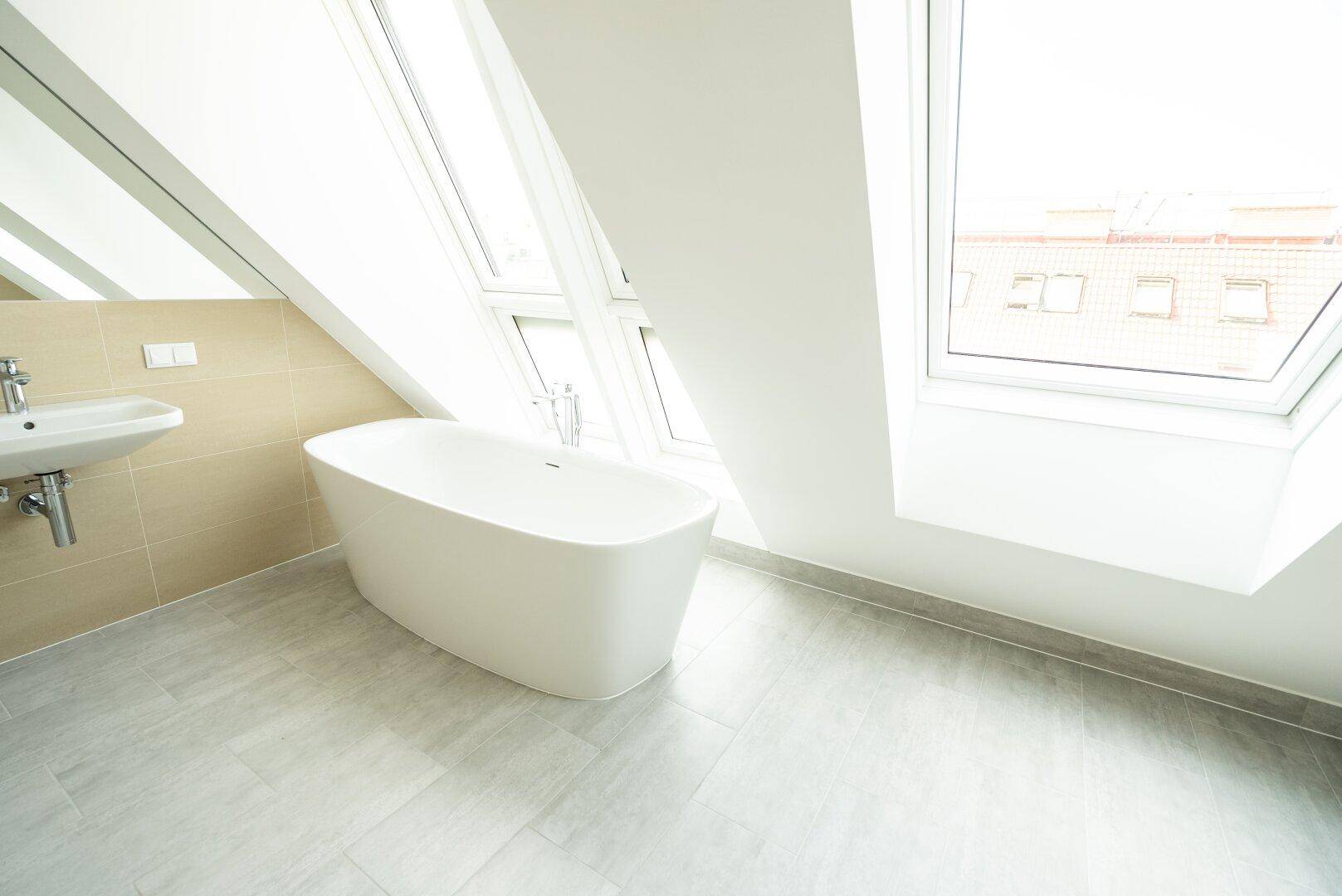 Helles Badezimmer im Dachgeschoss mit freistehender Badewanne und großen Dachfenstern.