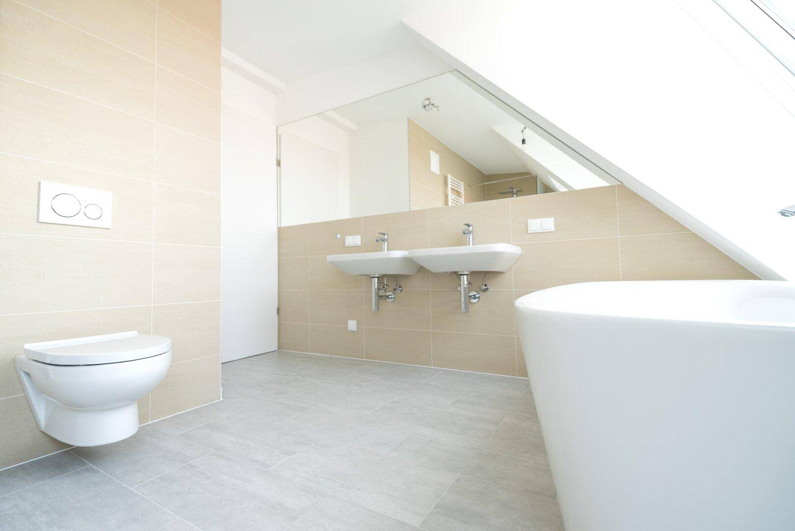 Modernes Badezimmer im Dachgeschoss mit Doppelwaschbecken, freistehender Badewanne und Wand-WC.