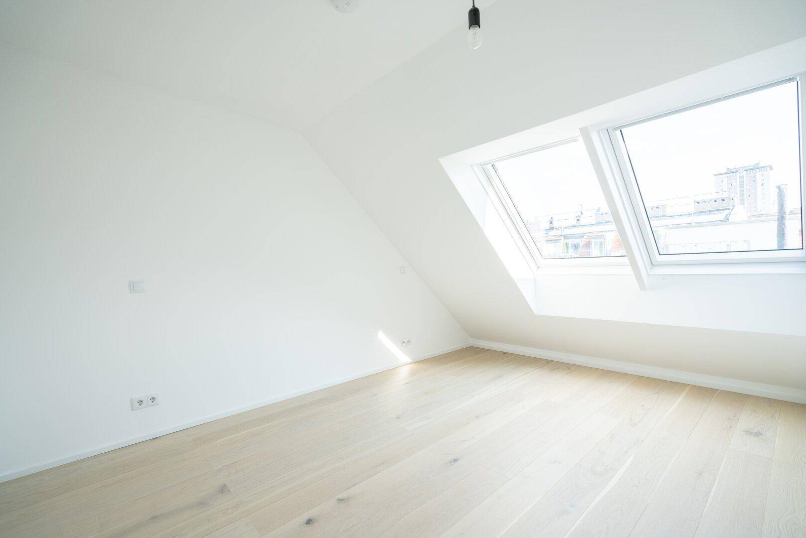 Helles Schlafzimmer im Dachgeschoss mit Holzboden und zwei großen Dachfenstern.