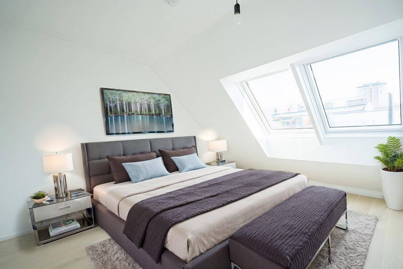 Modernes Schlafzimmer im Dachgeschoss mit großem Bett, schrägen Wänden und hellen Dachfenstern.