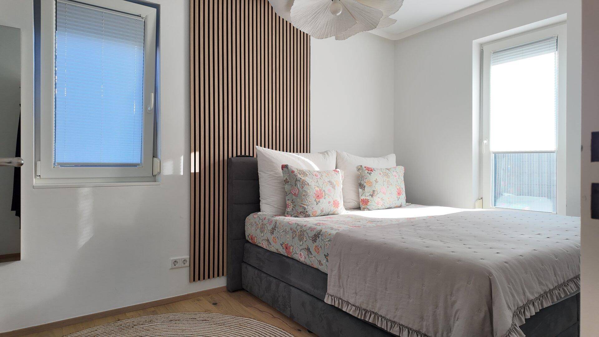 Helles Schlafzimmer mit modernem Bett, dekorativer Holzwandverkleidung und großem Fenster für viel Tageslicht.