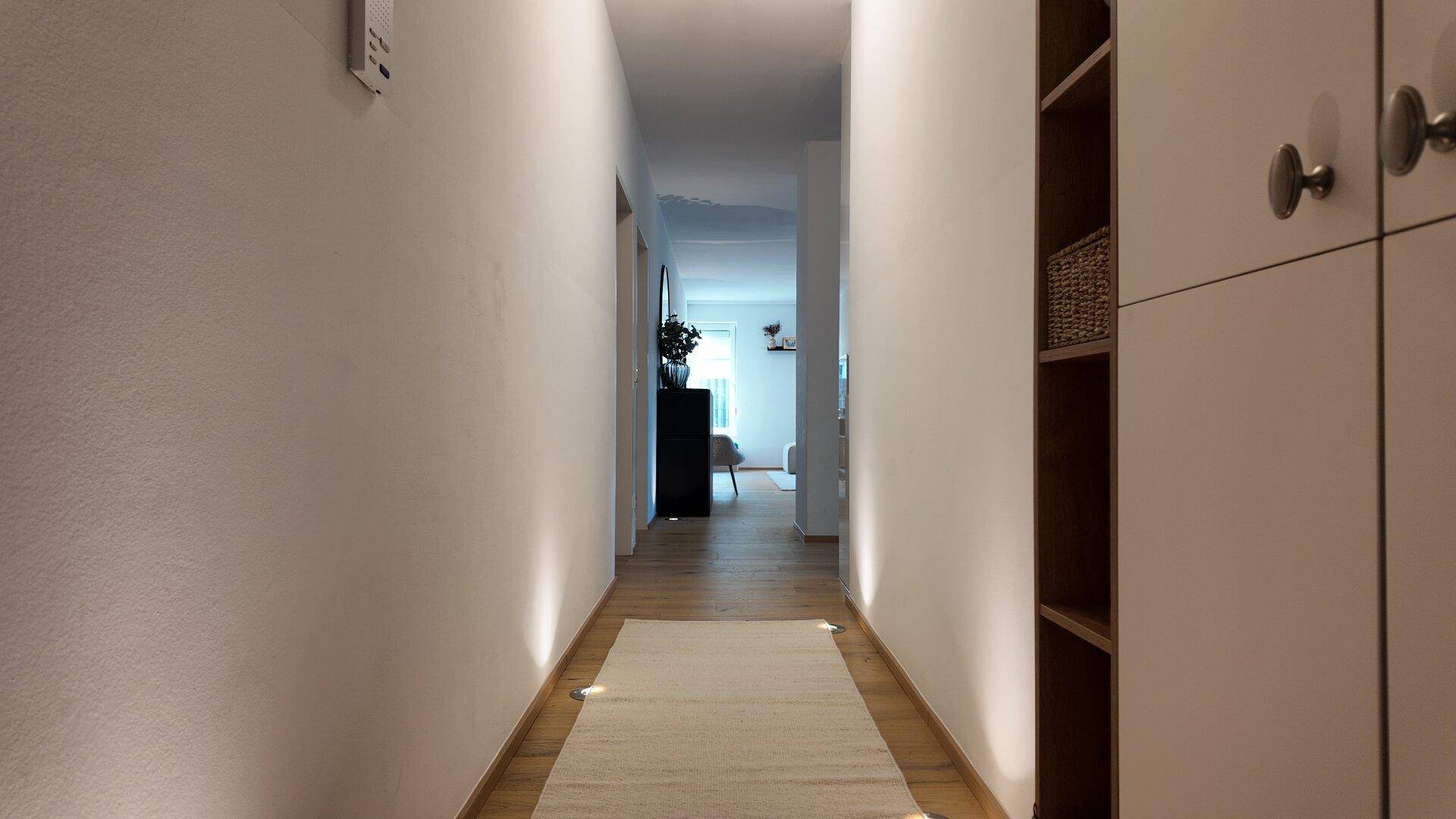 Langer, heller Flur mit Holzboden und indirekter Beleuchtung, der zu den Wohnbereichen führt.