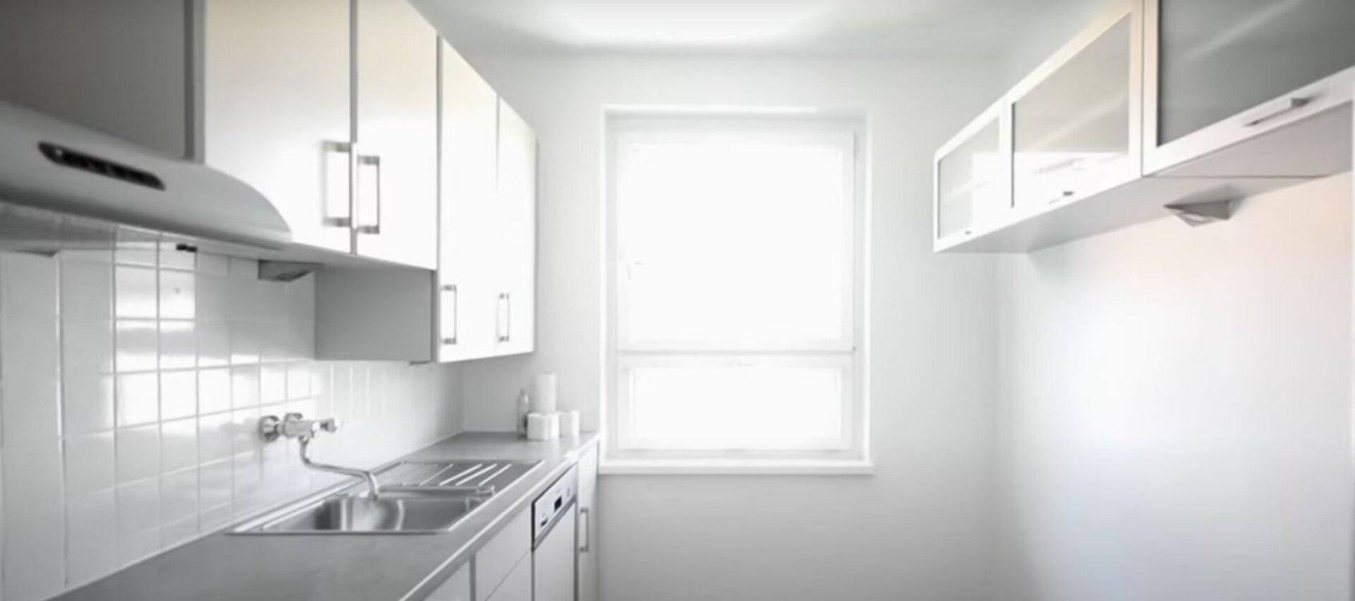 Funktionale Küche mit weißen Schränken, Spüle und einem Fenster, das natürliches Licht hereinlässt.