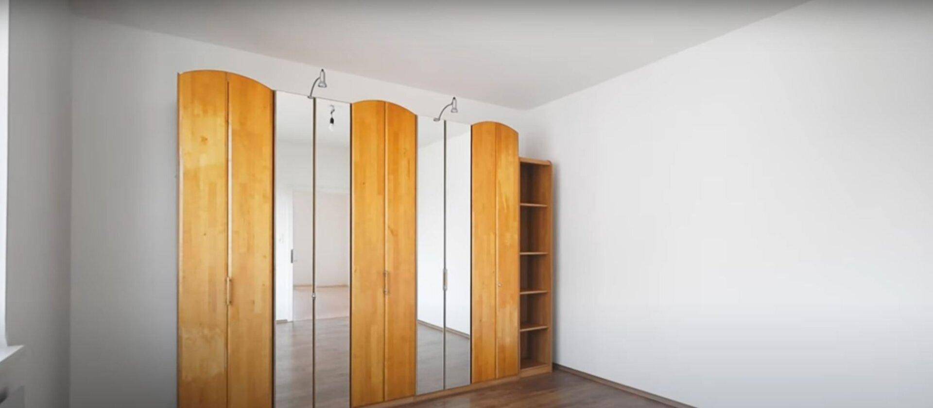 Geräumiger Raum mit einem großen Holzschrank mit Spiegeltüren und einem warmen Holzfußboden.