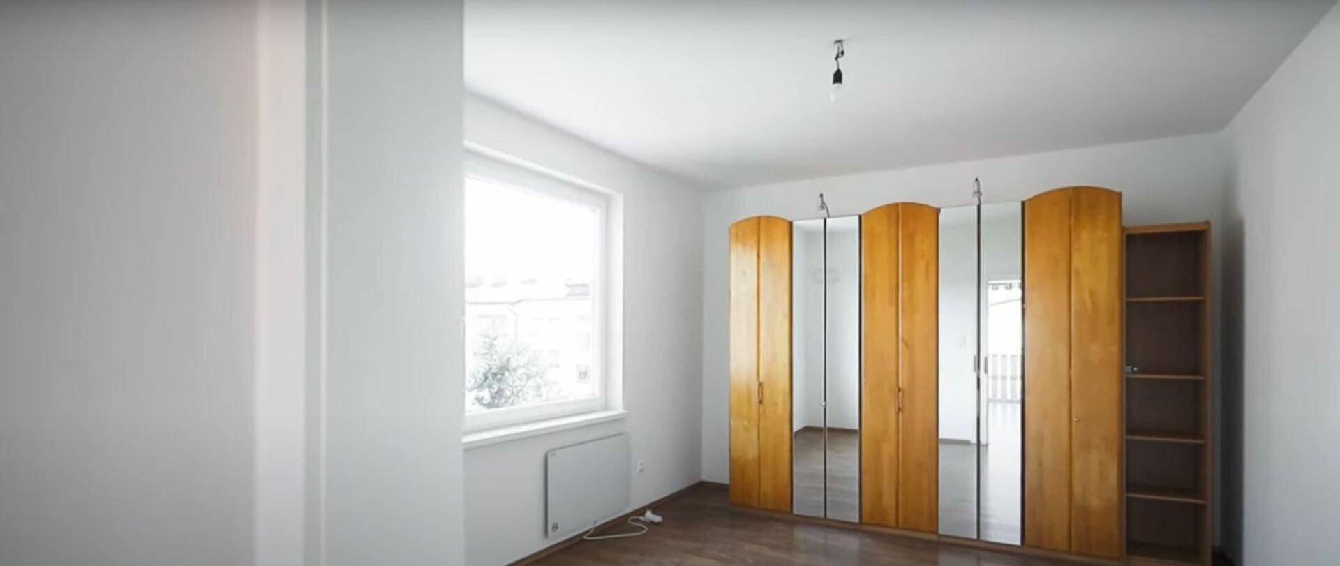 Heller Raum mit großem Fenster und einem Holzschrank mit Spiegelfronten und Holzfußboden.