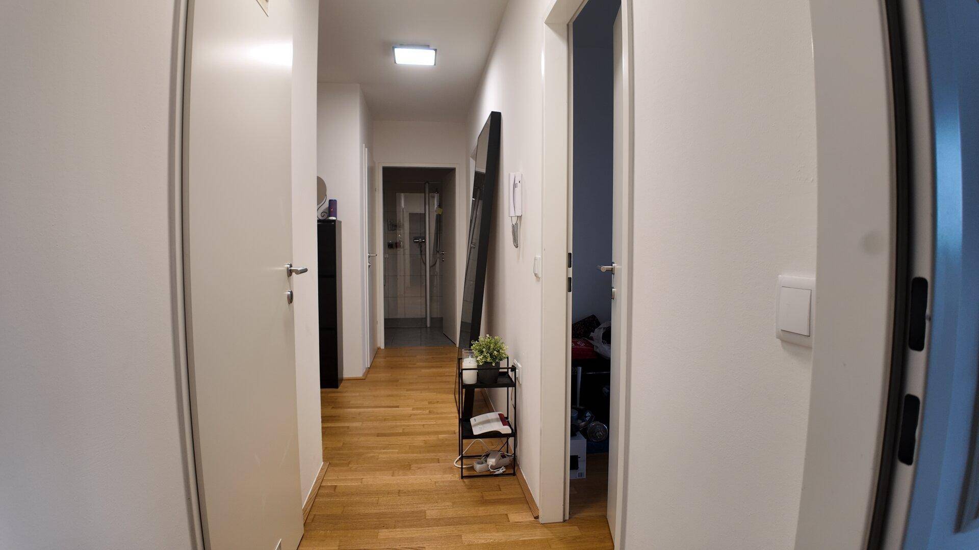Heller Flur mit Parkettboden, weißen Wänden und Zugang zu verschiedenen Räumen.