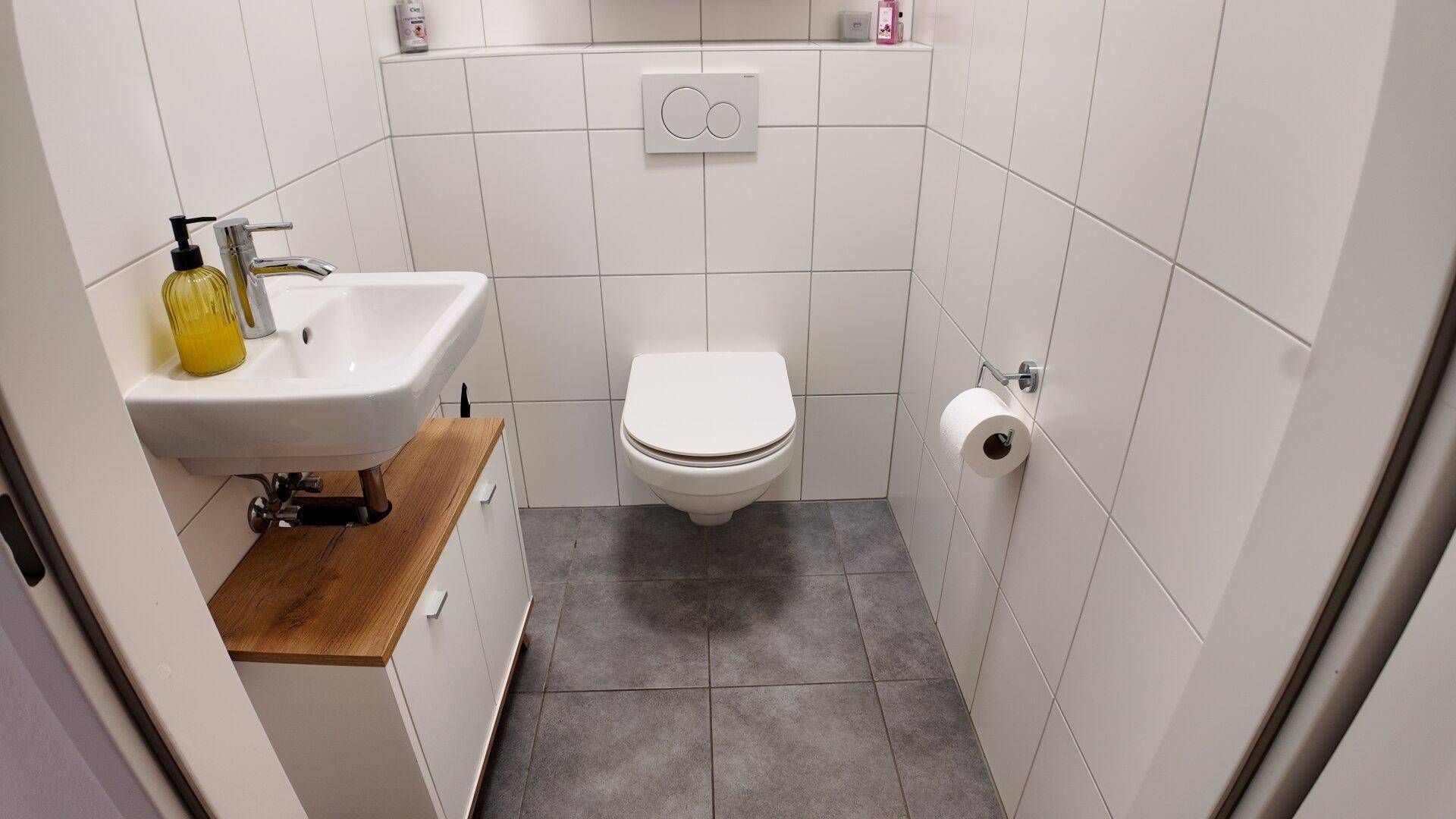 Kompaktes Gäste-WC mit Wand-WC, kleinem Waschbecken und Fliesenboden.