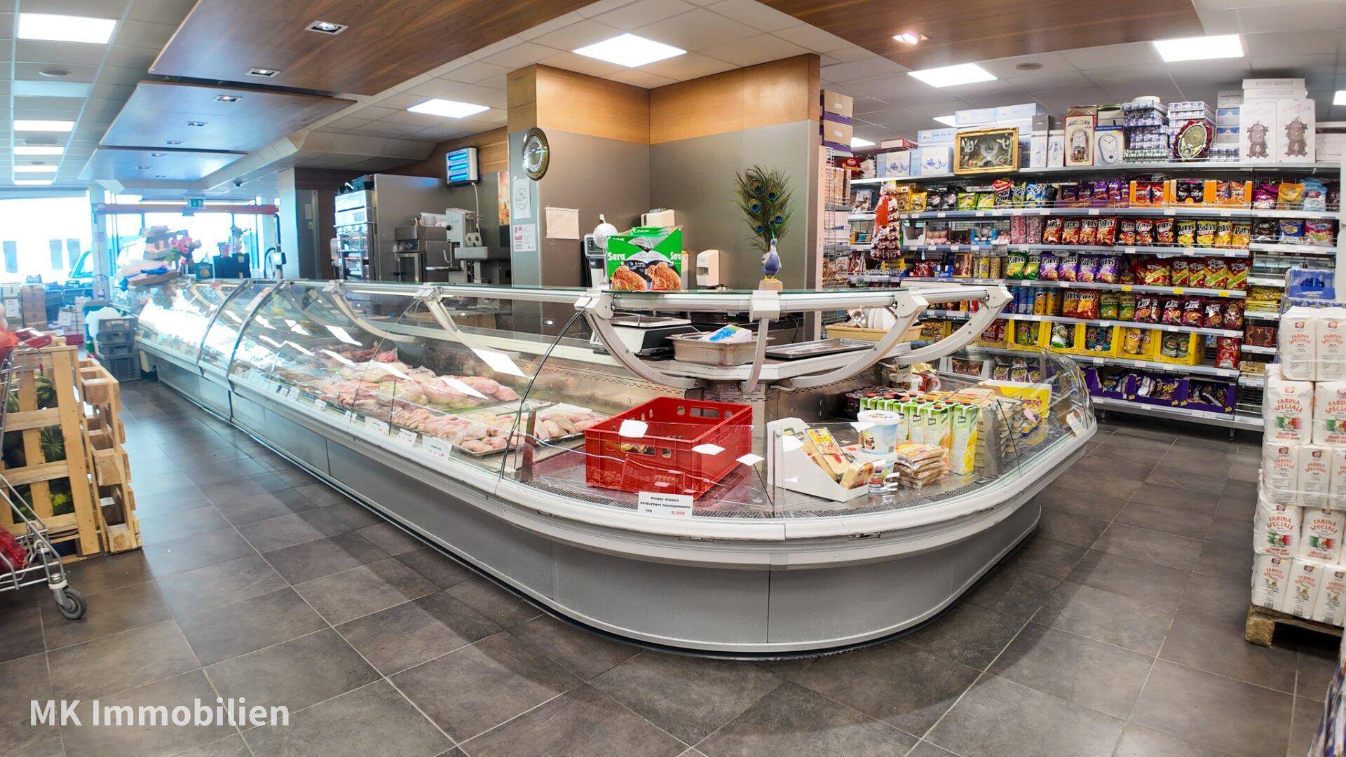 Große, geschwungene Frischetheke mit Fleisch- und Wurstwaren sowie weiteren Produkten in einem Supermarkt.