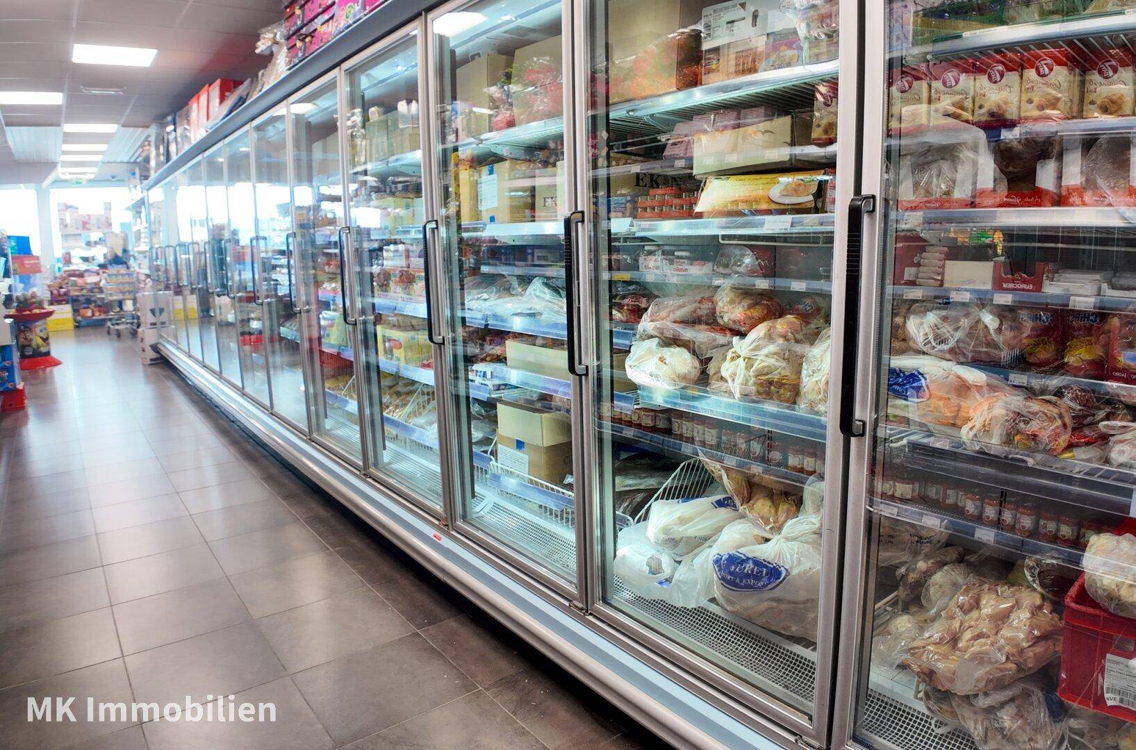 Lange Reihe von modernen Tiefkühlregalen mit Glastüren, gefüllt mit verschiedenen Produkten in einem Supermarkt.