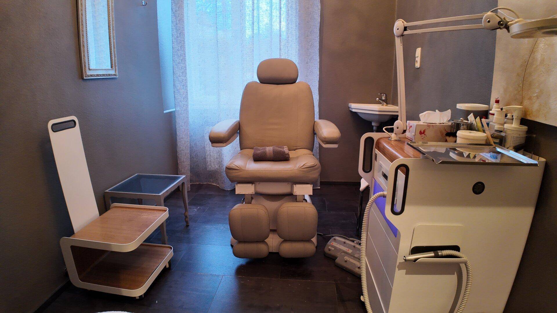 Behandlungsraum mit einem bequemen Therapiesessel, einem kleinen Waschbecken und moderner Ausrüstung.