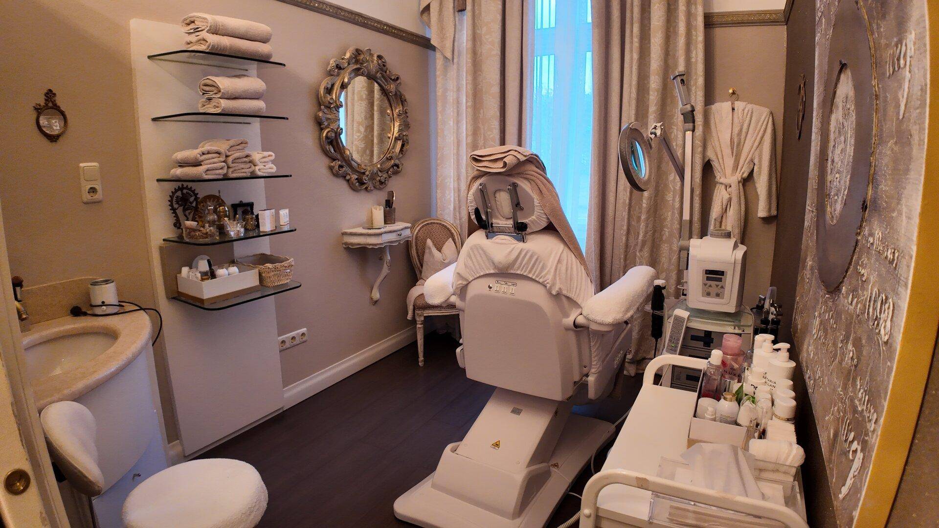 Heller Behandlungsraum mit einem Therapiesessel, Produktregalen und einem Fenster mit eleganten Vorhängen.