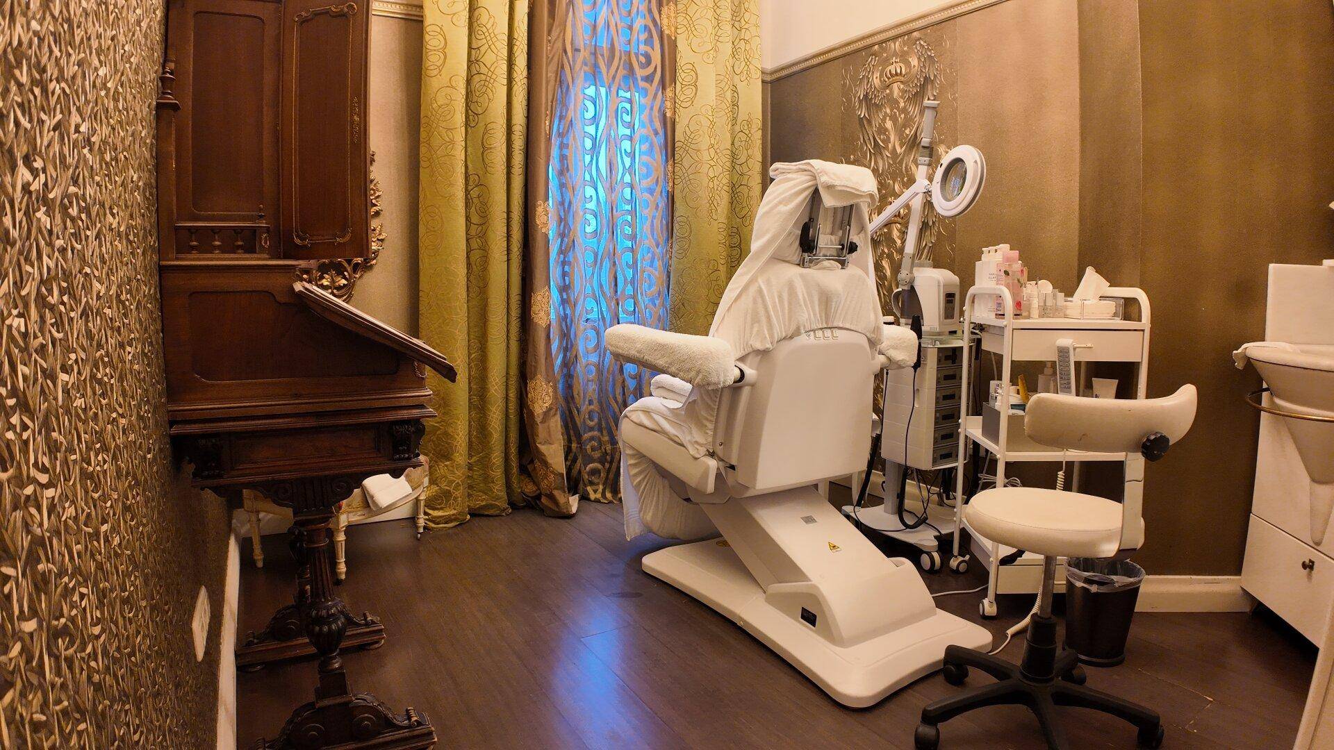 Eleganter Behandlungsraum mit einem Therapiesessel, einem antiken Schreibtisch und goldener Mustertapete.